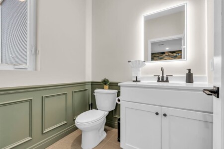 Bathroom sink, mirror, toilet with vase holding plant.