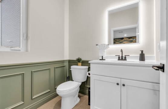 Bathroom sink, mirror, toilet with vase holding plant.