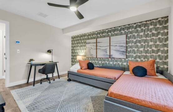 Two single beds with three framed pictures above, plus a side table and chair.