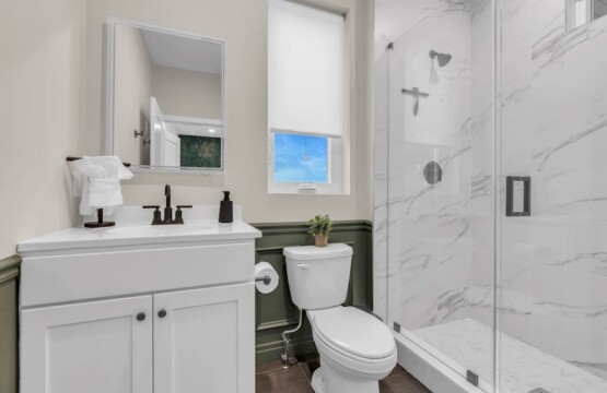 Bathroom with sink, mirror, toilet, towel holder above toilet, and shower visible.