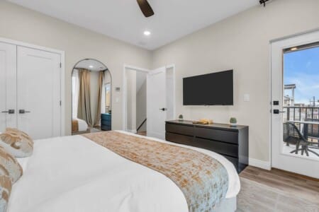 Bed facing the TV with a big mirror next to the bed and an open white door leading to the hallway.
