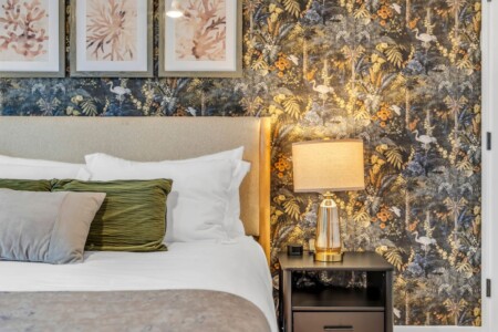 Bedroom bed with green decorative pillows and a side table holding a lamp.
