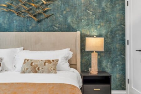Bedroom bed with green decorative pillows and a side table holding a lamp.