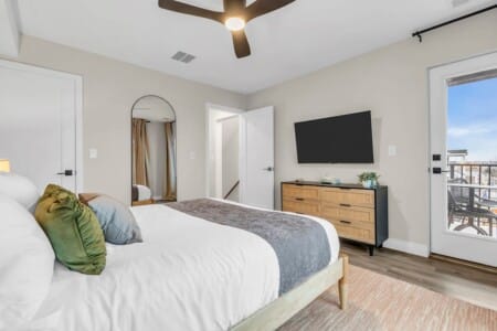 Bed facing the TV with a big mirror next to the bed and an open white door leading to the hallway.