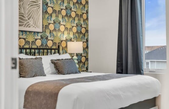 Bedroom bed with green decorative pillows, bedside table with lamp, and framed picture hanging on the wall.