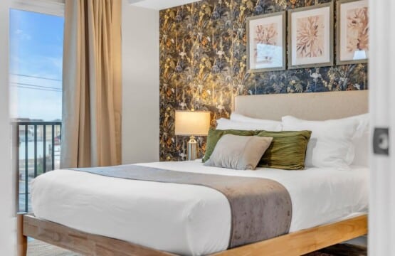 Bedroom bed with green decorative pillows, bedside table with lamp, and framed pictures hanging on the wall.