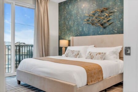 Bedroom bed with green decorative pillows, bedside table with lamp, and beutiful sky view.