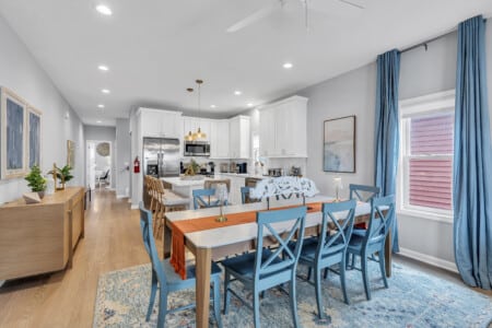 Dining area with large table, white kitchen view, two framed pictures on the wall.