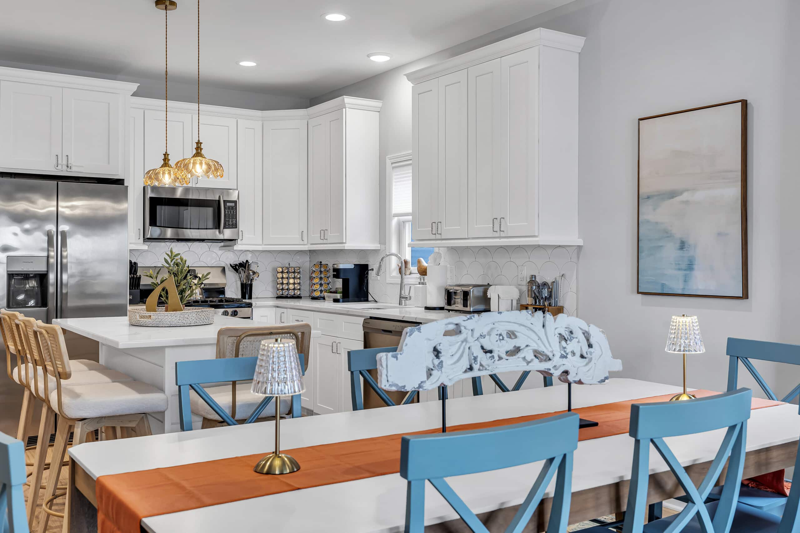 Dining area with large table, white kitchen view, two framed pictures on the wall.