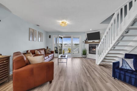 Spacious living room with white stairs, two brown couches, TV on the wall, and waterfront view.