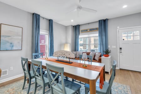 Dining area with brown bed, white windows with blue curtains and a beautiful framed see drawing on the wall.