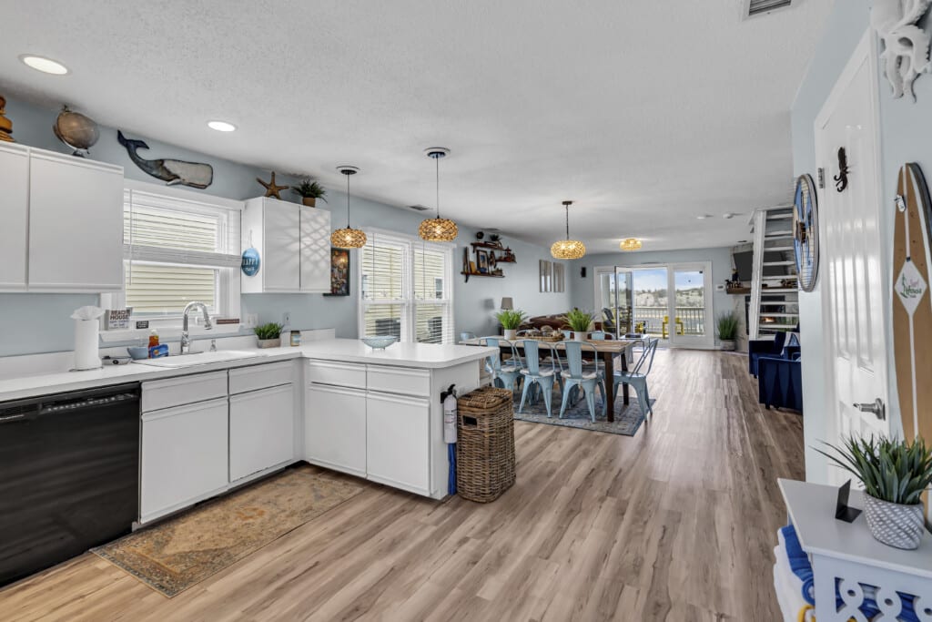 White kitchen opening to living room with large windows showing a waterfront view.
