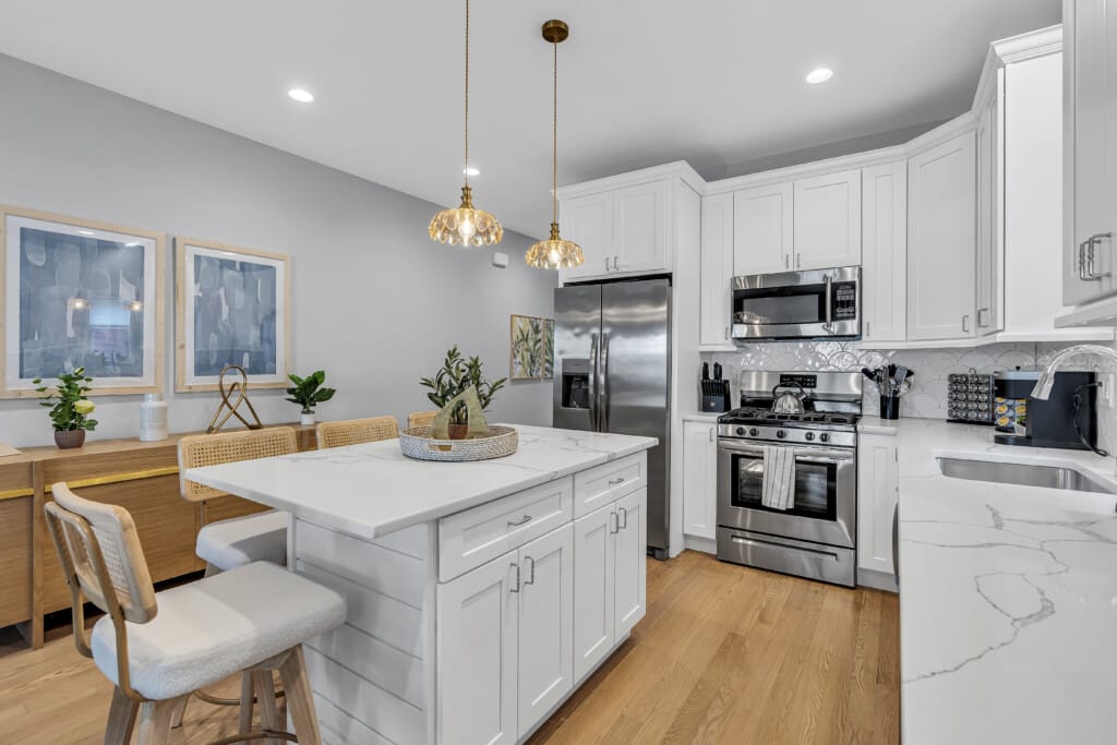 Bright white kitchen featuring a flower vase placed in the middle of the table, two framed drawings on the wall.