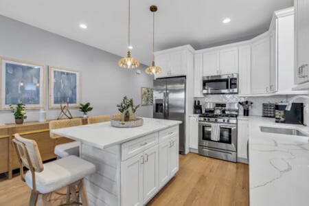 Bright white kitchen featuring a flower vase placed in the middle of the table, two framed drawings on the wall.