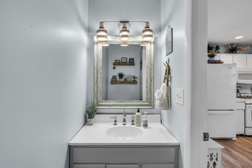 View facing bathroom mirror and sink with hand soap, and kitchen fridge visible next door.
