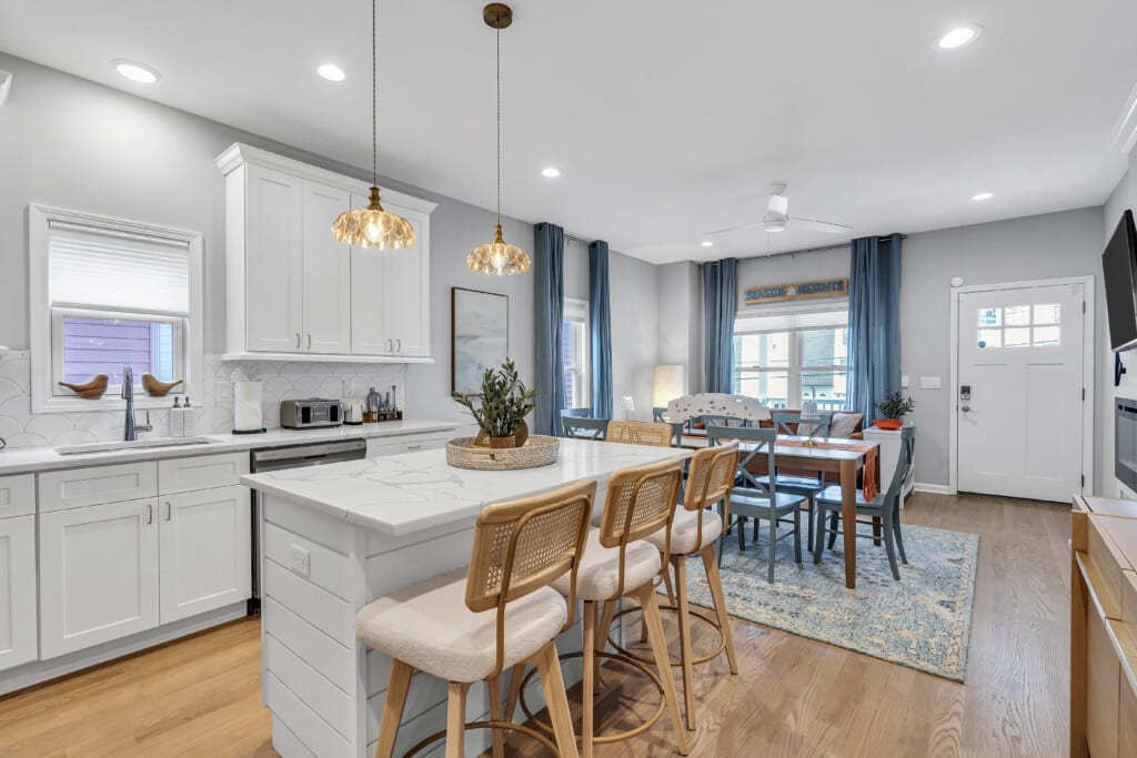 Dining area with large table, white kitchen view, two framed pictures on the wall, and a wall-mounted TV.