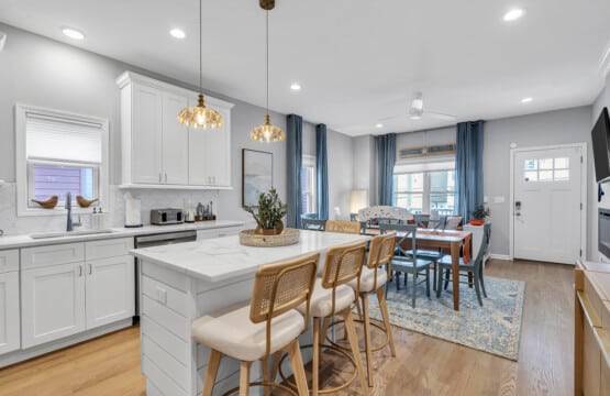 Dining area with large table, white kitchen view, two framed pictures on the wall, and a wall-mounted TV.