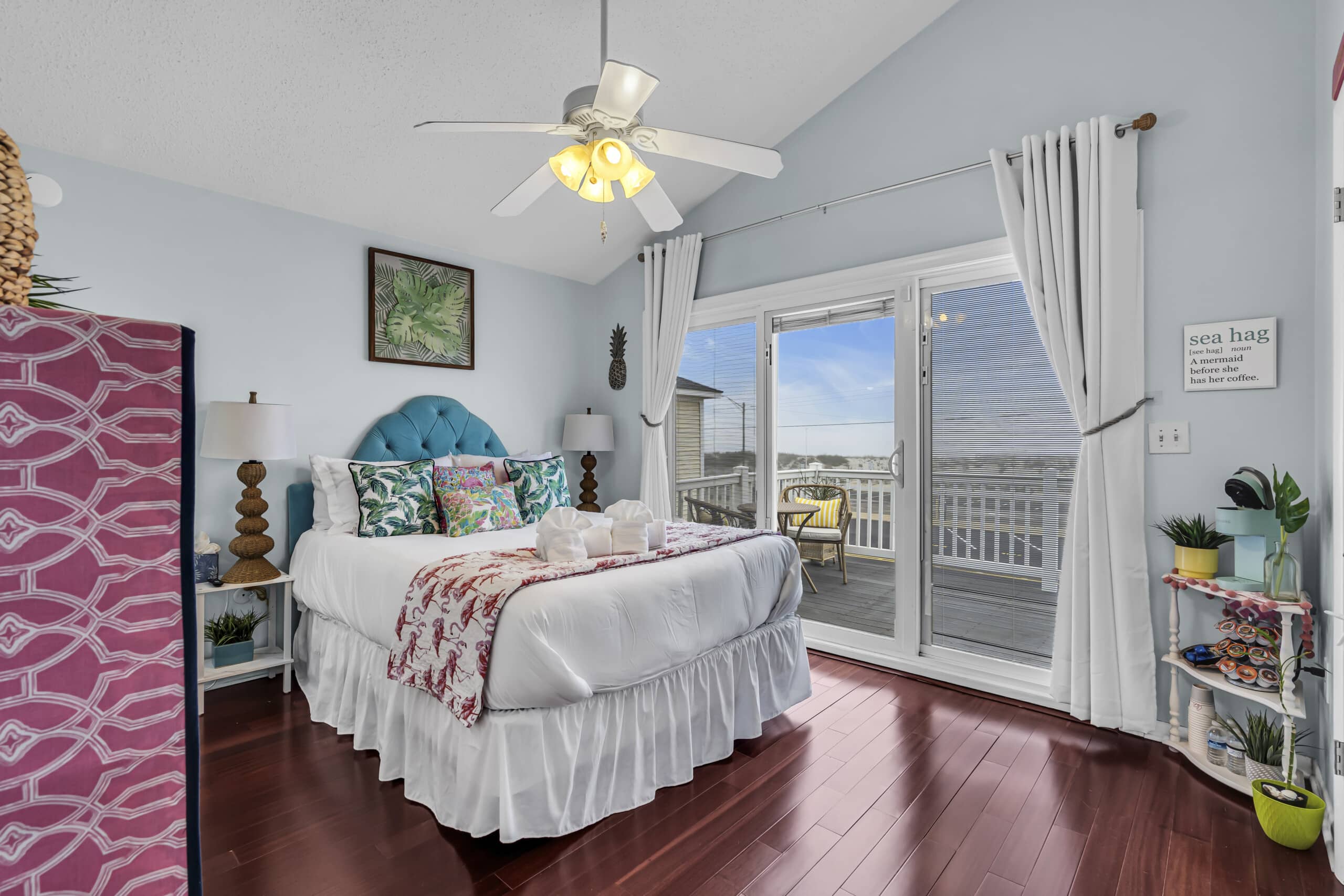 Bedroom with balcony view, framed artwork on the wall, and decorative plants in the corner.