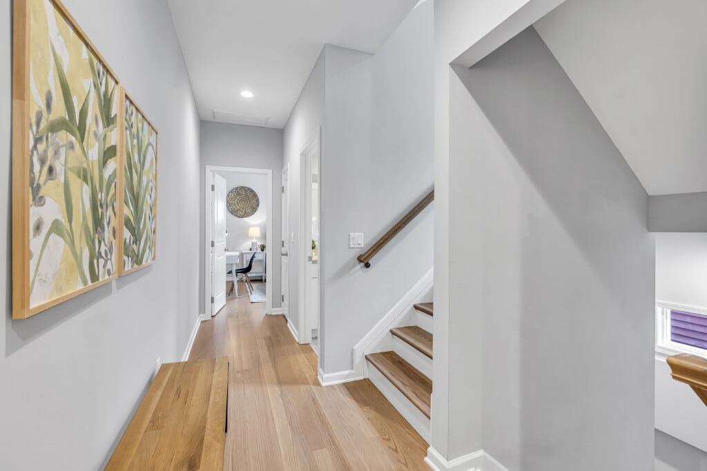 Hallway with two framed drawings on the wall, stairs, and a bedroom visible next door.