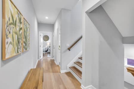 Hallway with two framed drawings on the wall, stairs, and a bedroom visible next door.