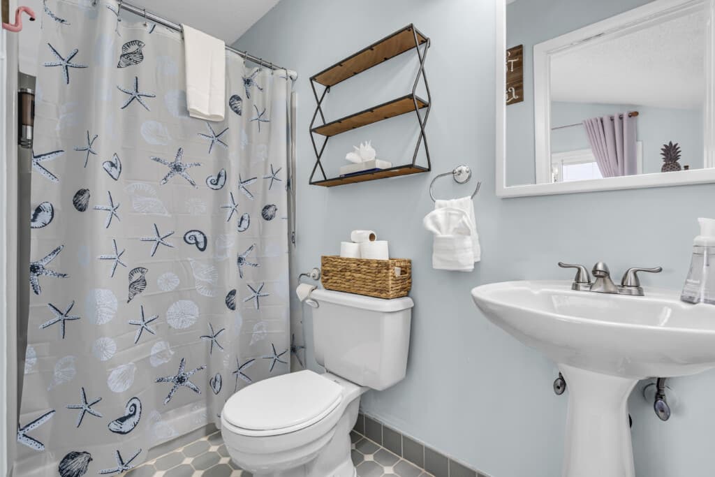 bathroom with toilet, sink with hand soap on it, mirror on the wall and shower covering curtain.