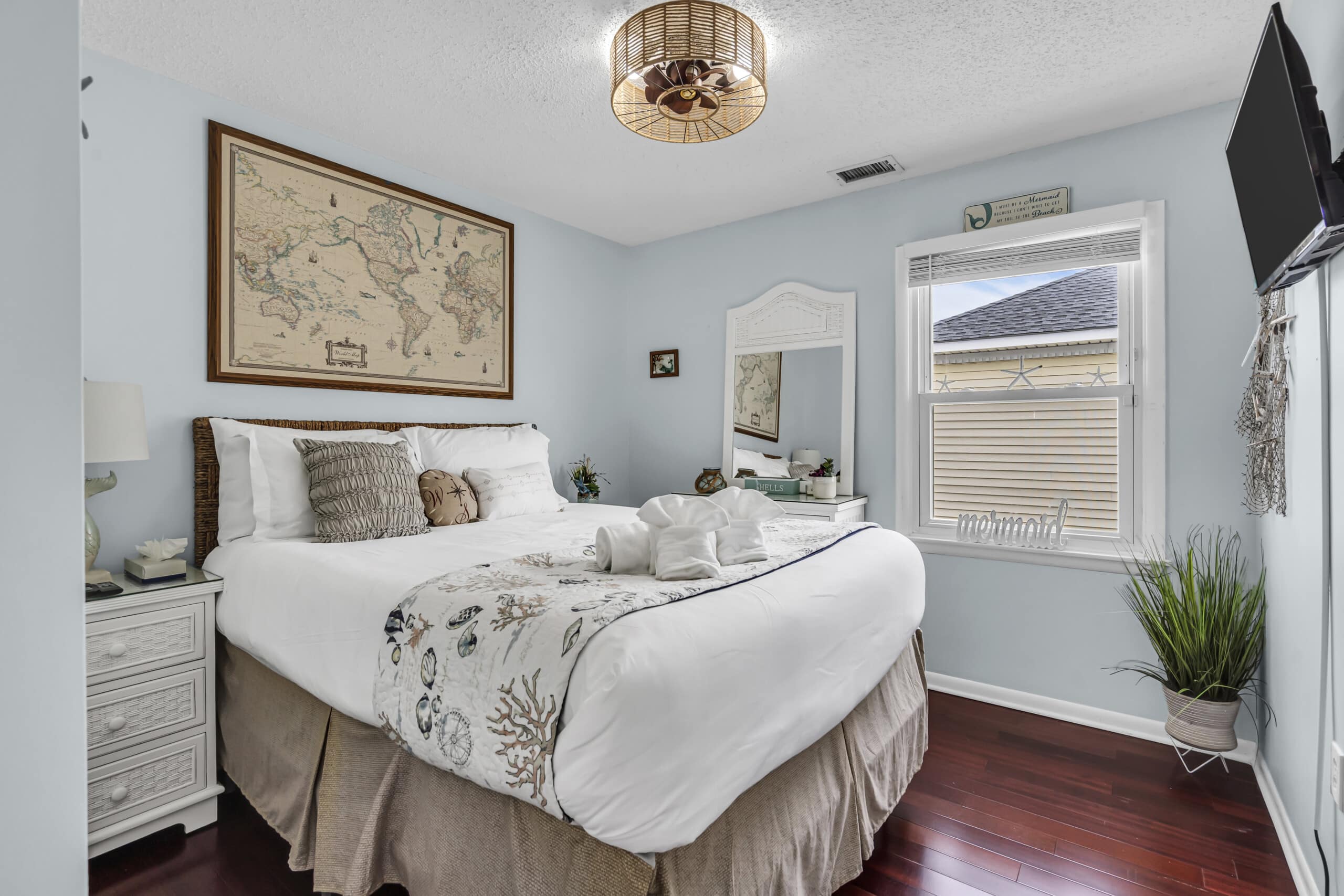 Cozy bedroom see print covered bed, wall mirror, tv on the wall, and open window.