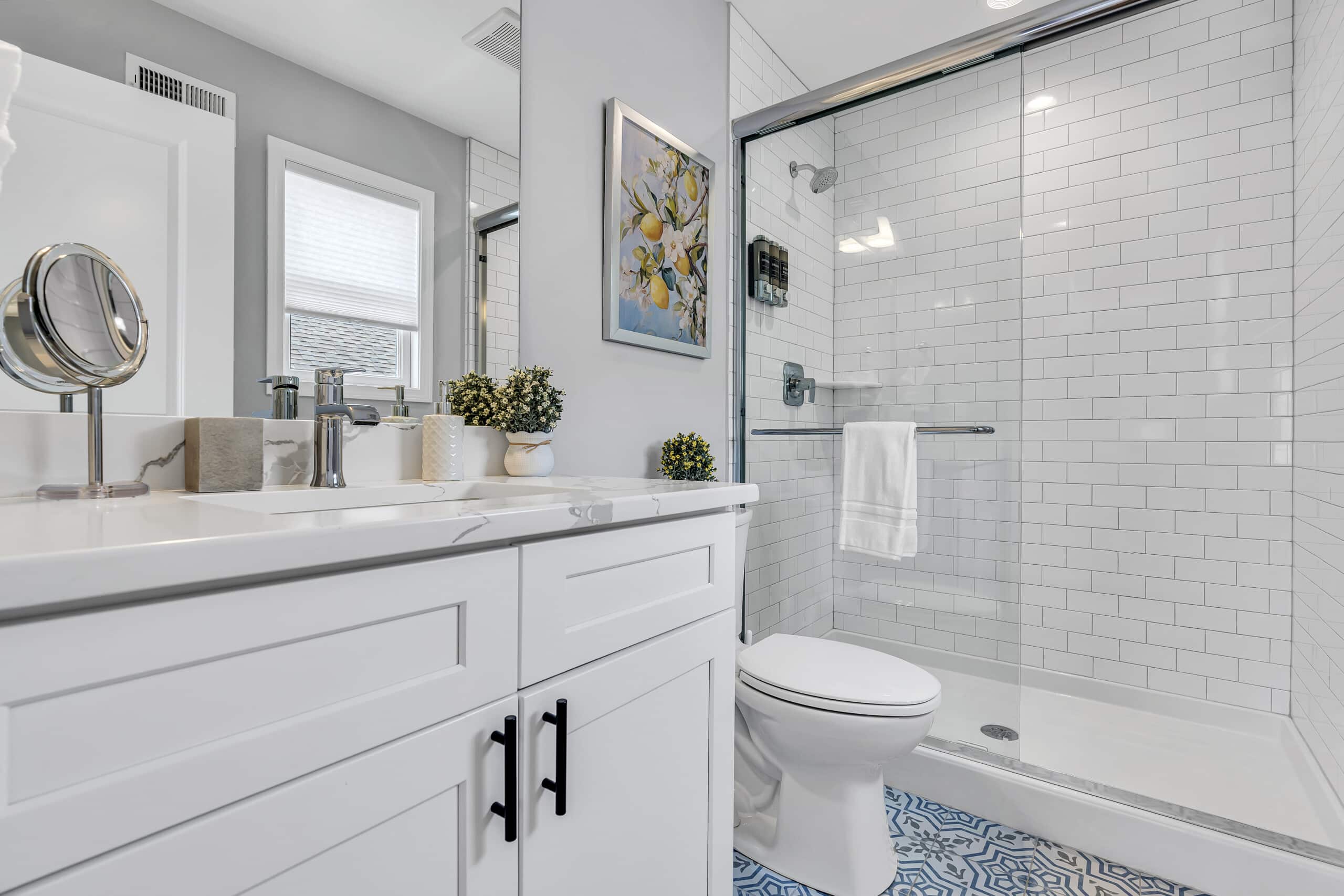 Well-lit bathroom featuring white sink, decorative flowers, mirror, and white tiles shower.