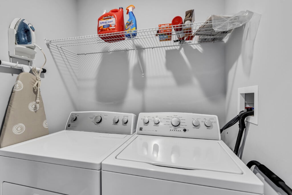 Small laundry room with dryer and washing machine, iron and ironing board on wall.