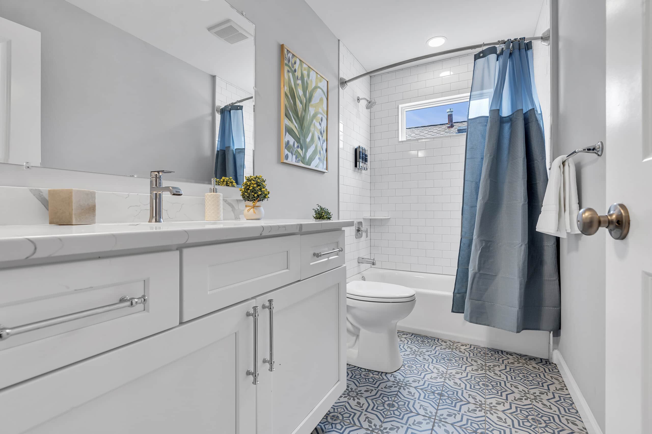Well-lit bathroom featuring white sink, decorative flowers, mirror, and shower with window covered by blue curtain.