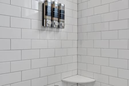 Close-up of white shower tiles with three shampoo bottles hanging inside.