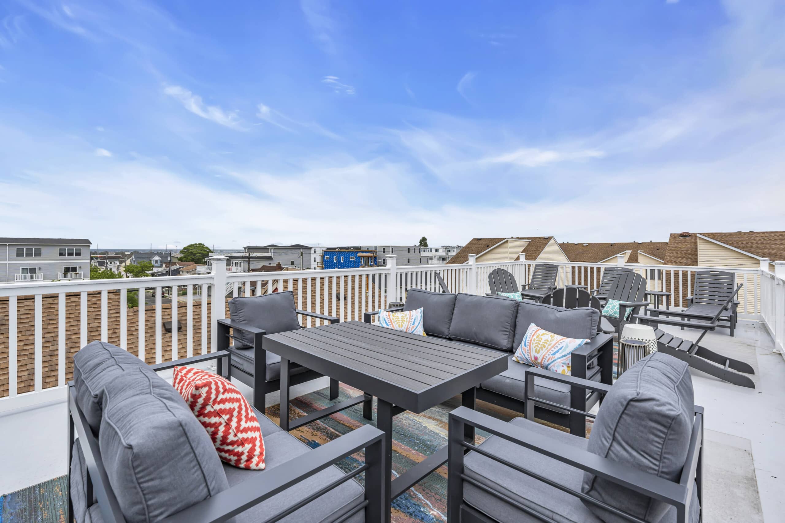 Sunny balcony with white fence, table, chairs, and a clear view of the Jersey neighborhood below.