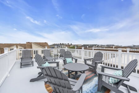 Bright balcony with white fence, table, and chairs offering a sunny view of a Jersey neighborhood.
