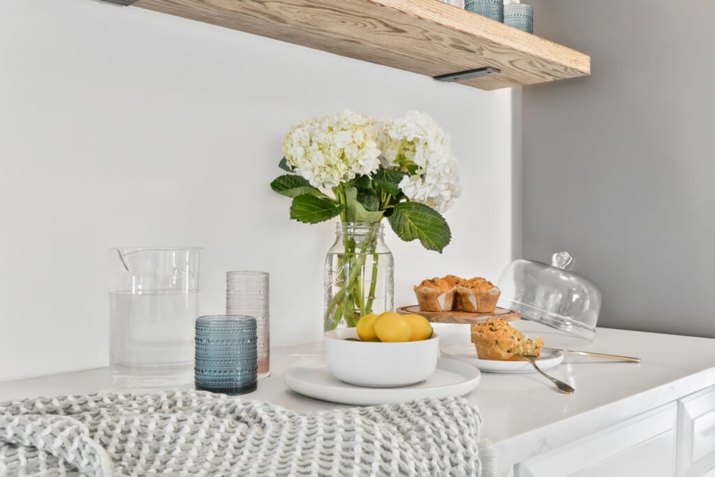 Table setting with water glass, tasty muffins, plate of lemons, and a vase of white flowers.