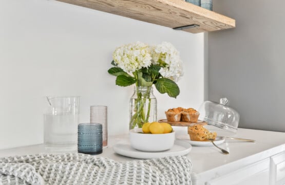 Table setting with water glass, tasty muffins, plate of lemons, and a vase of white flowers.