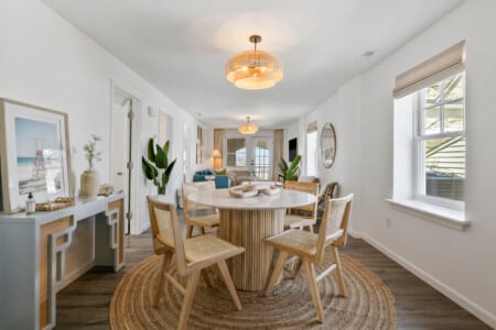 Living room with balcony view, blue couch, two white chairs, round mirror, open window, and dining table nearby.