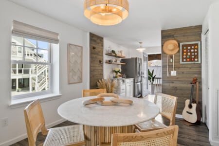 Dining room with table, kitchen view, grey fridge, guitar in corner, and hat hanging on the wall.