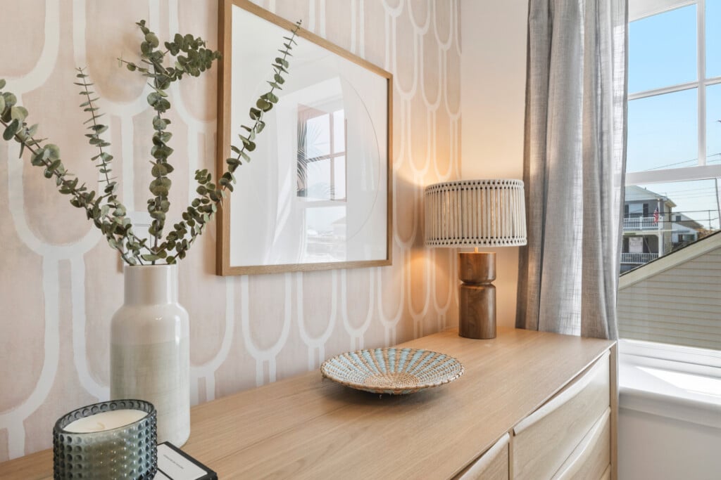 Close-up of brown table with plant vase, white lamp, candle, wall picture, and window in the corner.