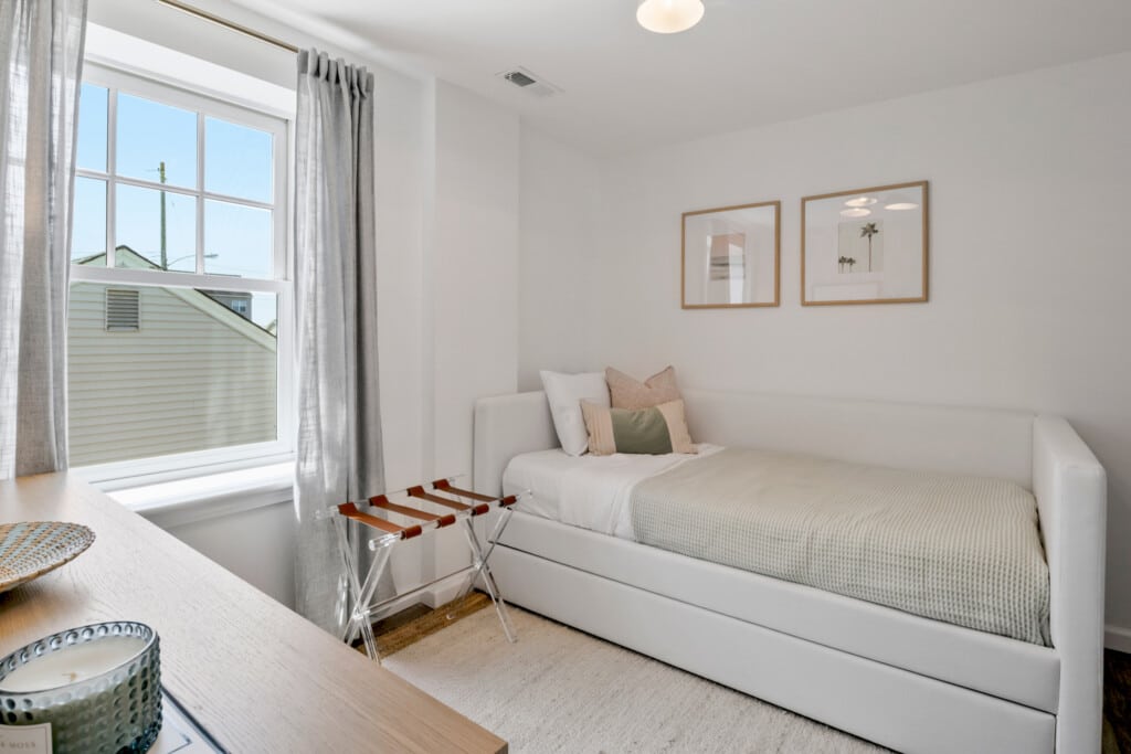 White room with single bed and pillows, white window, and a candle placed on the bedside table.
