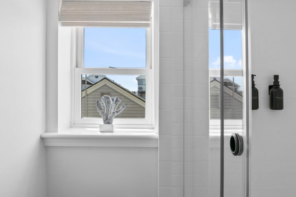 Close-up of shower with two black shampoo bottles and a white window showing neighborhood view.