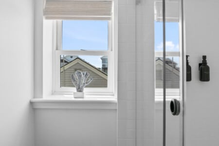 Close-up of shower with two black shampoo bottles and a white window showing neighborhood view.