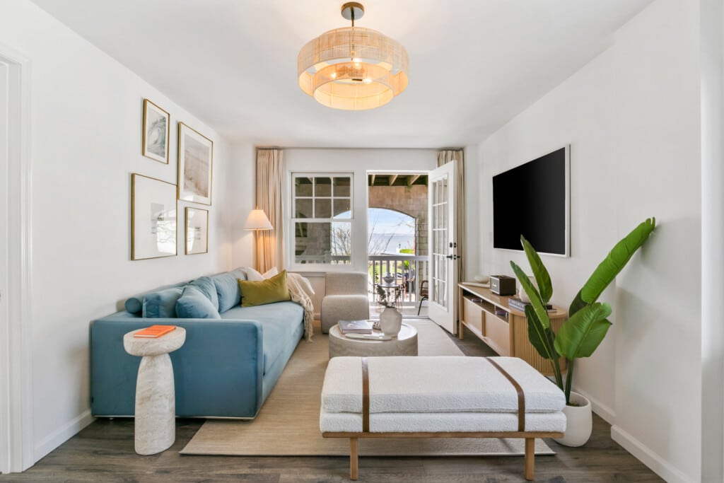 Cozy living room with balcony view, comfy blue couch, white sofa, and vase with book on the table.