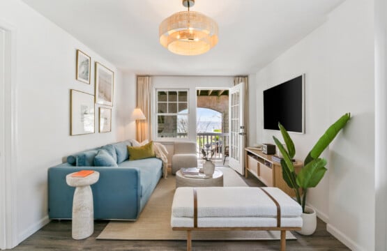 Cozy living room with balcony view, comfy blue couch, white sofa, and vase with book on the table.