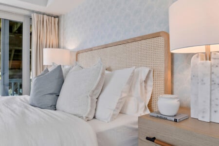 Close-up of white pillows with bedside table holding lamp, Balenciaga book, and small vase decoration.