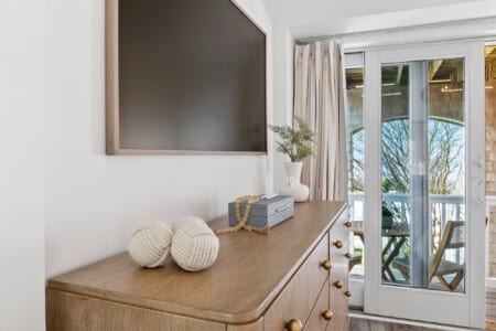 Close-up of TV on wall with table below, decorated with a box and a vase holding green plant.