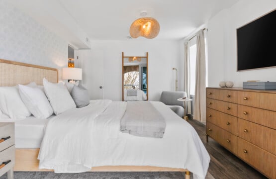 Bedroom with white bed, grey sofa, large wall mirror, and TV mounted opposite the bed.