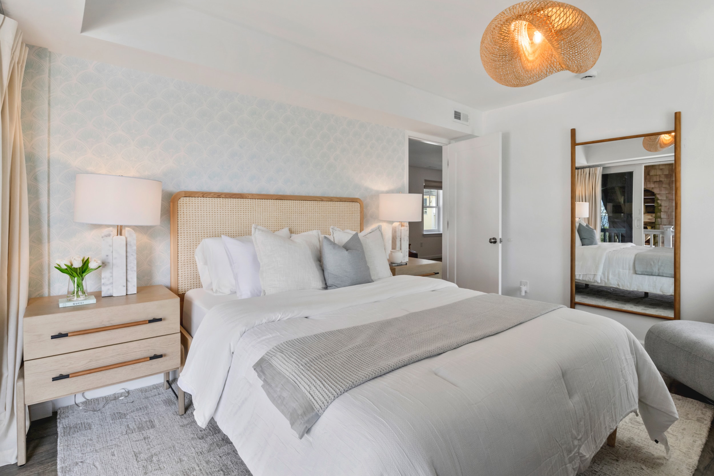 Bedroom with white bed, large wall mirror, two lamps on each side, and a vase with white flowers.