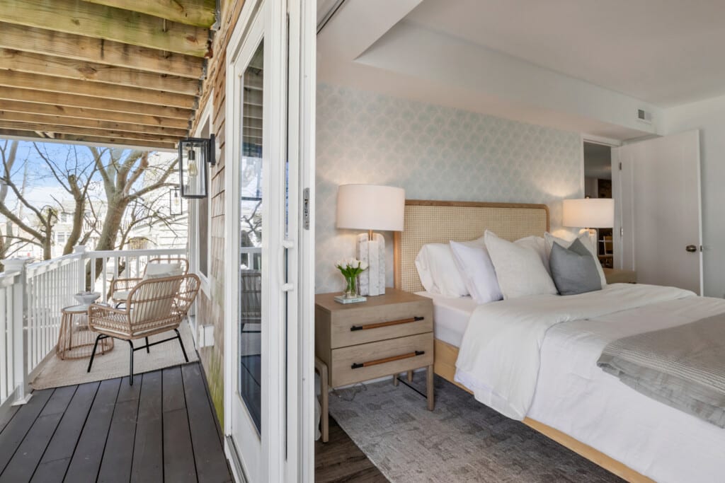 Half of a cozy bedroom and half of a balcony with chairs, table, vase, plant, and white fence.