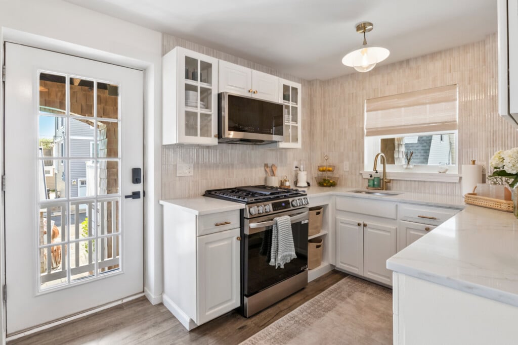 White kitchen with window, electric stove holding towel, lemons on the kitchen table and white door with garden view.