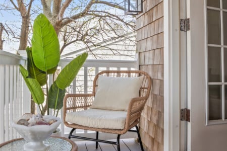 Cozy balcony with a cushioned wicker chair, potted plant, and a bowl of seashells on a glass table.