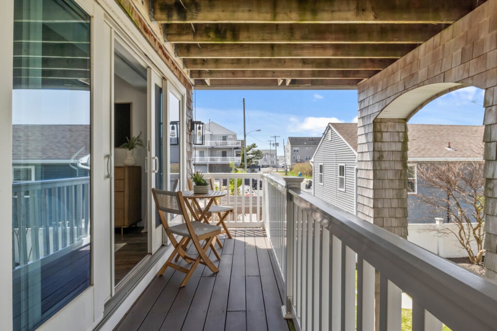 Sunny balcony with two chairs, a table with a plant, and a beautiful view of the neighborhood.